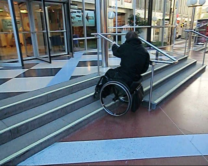 Kommer uppför en trappa med ledstång med rullstol